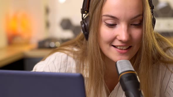 Young smiling woman with headphones recording podcast using laptop at home studio.
