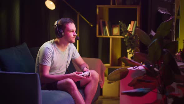 Young Man Gamer Wearing Headphones with Microphone Playing Video Game on Tv Gesturing