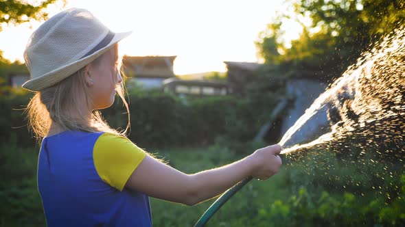 Funny Little Girl in Hat Playing with Garden Hose in Sunny Backyard. Adorable Little Girl Playing