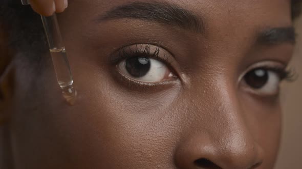 Black Woman Applying Facial Serum With Dropper Beige Background Closeup