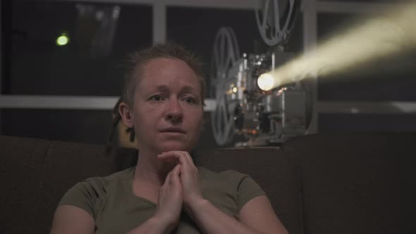 Woman watching dramatic movie on old film movie projector in dark room