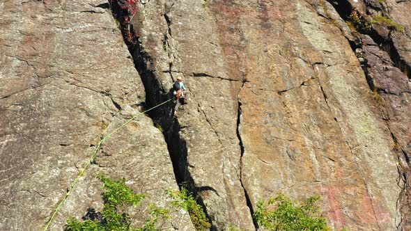 Aerial footage tilting up past lone climber on cliff in Maine