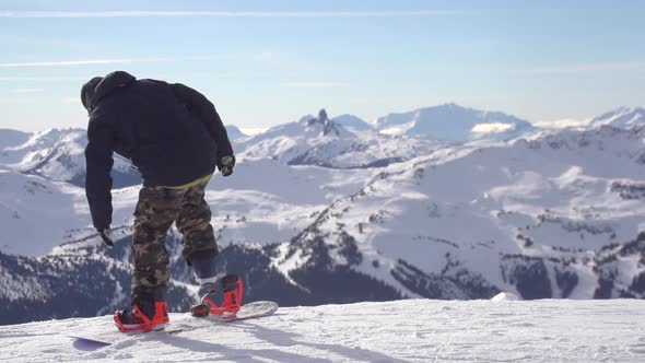 A young man snowboarder standing with his snowboard on a snow covered mountain.