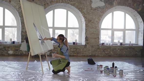 Female Artist Working with Large Paintbrush and Wide Canvas in Workshop