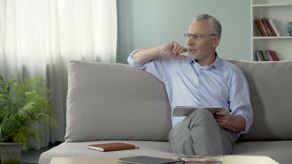 Adult Male Sitting on Couch and Booking a Hotel Room for Vacation on Tablet