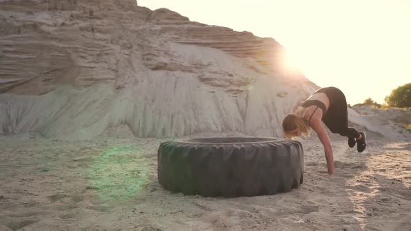 Girl on Sand Quarry Jumping Burpee with push-UPS Through the Wheel in the Sand