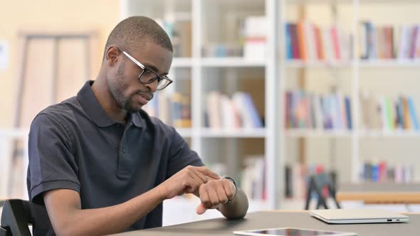 Bored Young African Man Using Smartwatch in Library