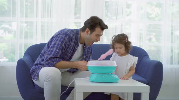 Hand father rolling cotton candy in candy floss machine and eat cotton candy together with daughter