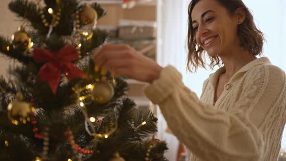 Close Up Slow Motion of Beautiful Smiling Woman Decorates Christmas Tree at Home with Bulbs