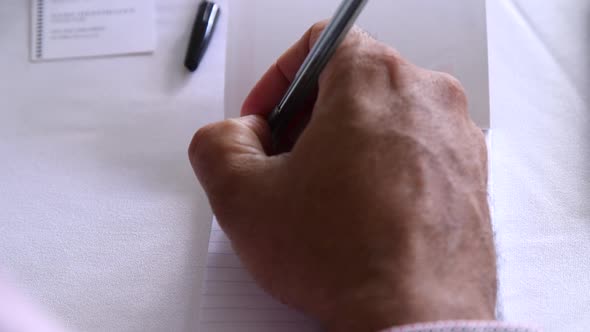Close up of male hands writing on a pad of white paper with a pen