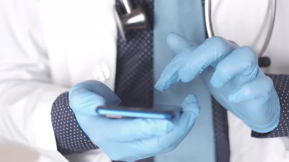 Doctor's Hand in Protective Gloves Using a Smartphone