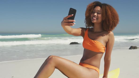 African American woman sitting on her surfboard taking selfie