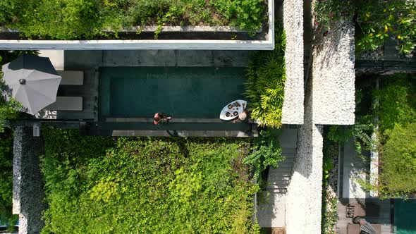Aerial top down view of a young couple poolside at a luxury tropical villa with a floating breakfast