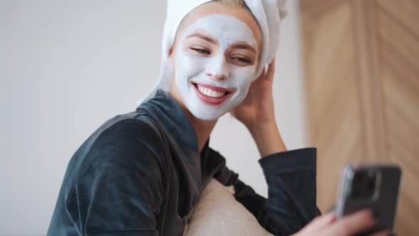 Positive blond woman with a towel on her head looking at phone