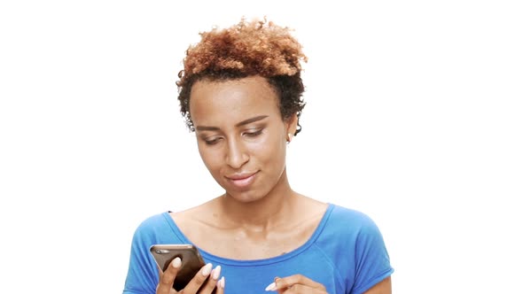 Young Beautiful African Girl Looking at Phone Dancing Smiling Over White Background