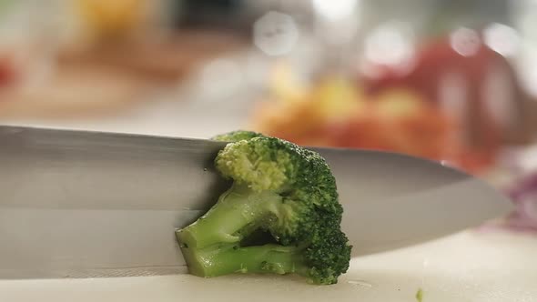 close-up of steel blade of kitchen knife slicing through frozen broccoli.