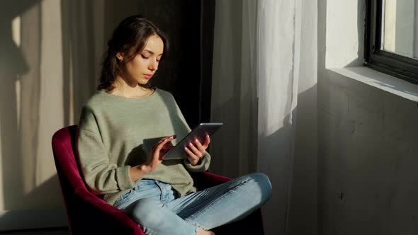 Beautiful Woman Sitting Near Window and Using Her Tablet at Sunrise