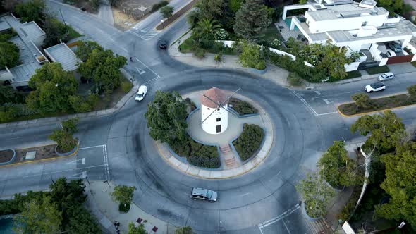 Aerial orbit of Leonidas Montes windmill tower in roundabout with cars driving surrounded by trees,