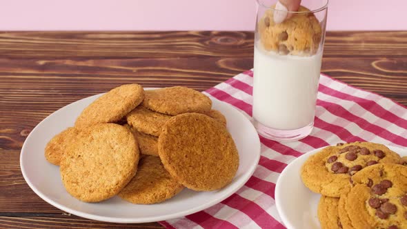 Female Hand Dipping Chocolate Chip Cookie Into Milk Glass on Wooden Table