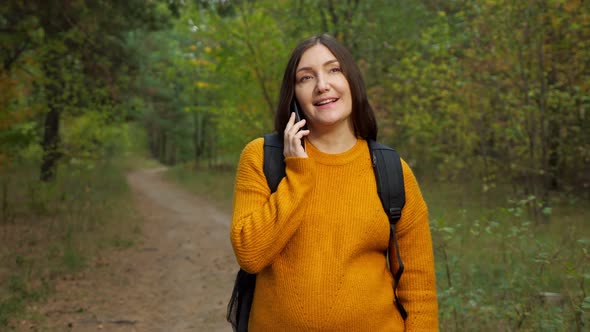 Smiling Lady Traveler Talks on Smartphone in Autumn Forest