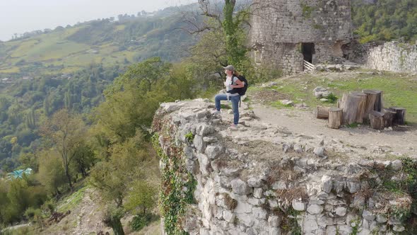 Flyby of tourist girl standing on edge of cliff in mountains