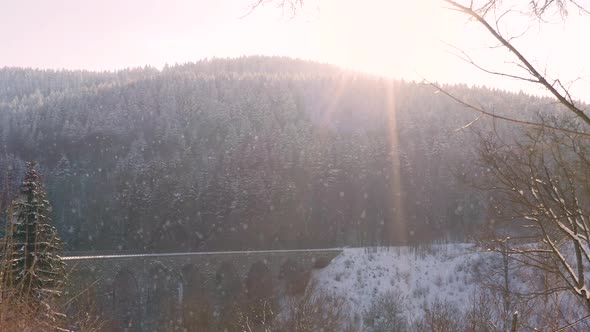 Sun shining on a railway viaduct over a mountain valley,falling snow.