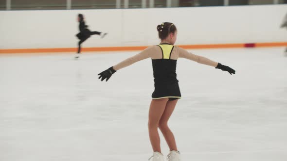 Little Girl Figure Skater in Training Black and Yellow Costume Skating on the Public Rink and