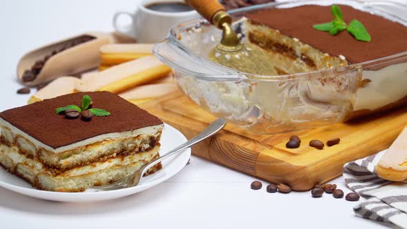 Traditional Italian Tiramisu dessert in glass baking dish, portion on plate and cup of coffee