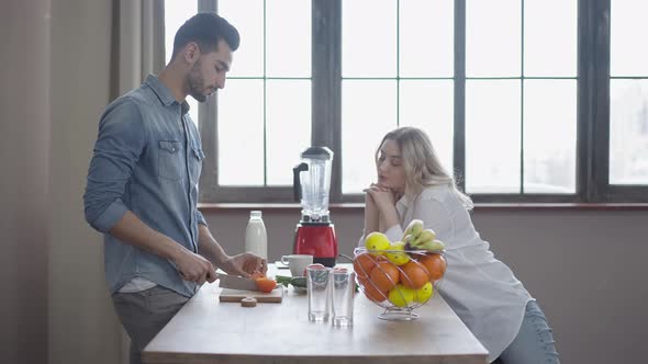 Happy Interracial Couple Talking and Laughing Cooking Healthful Salad at Home