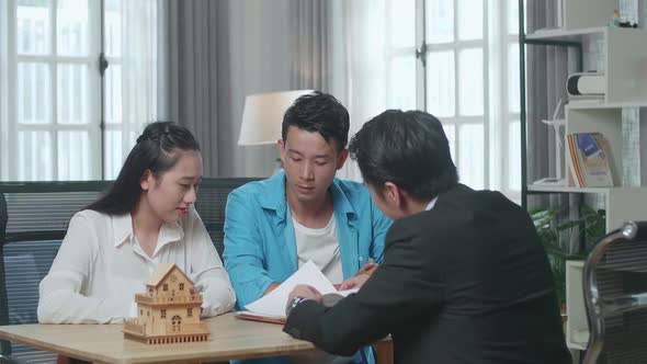 Asian Couple Listens To A Real Estate Agent Explaining About House Purchase Contract At The Office