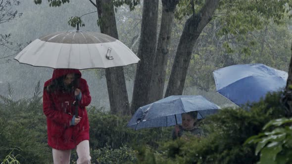 Kids in the pouring rain having fun jumping with umbrellas - slow motion