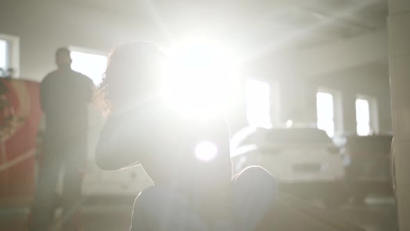 Portrait of Young Caucasian Female Auto Mechanic Sitting in Sunrays in Auto Repair Shop. Charming