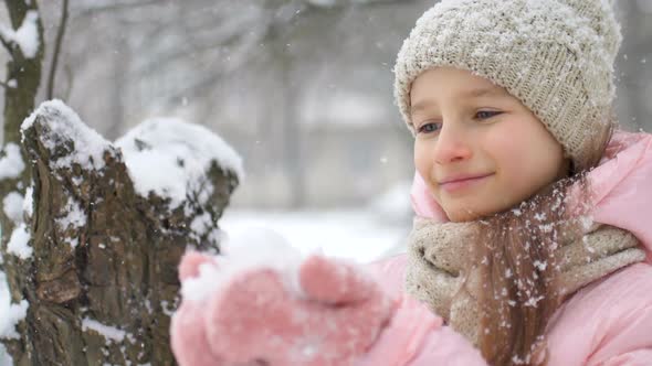 Winter Portrait of a Kid Girl in Pink Coat Wearing Beige Hat and Mittens Playing Outdoor in Snowy