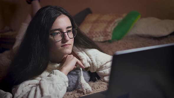 Cute girl lies on bed with laptop