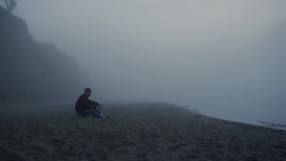 Depressed Guy Sitting Sea Beach in Foggy Morning