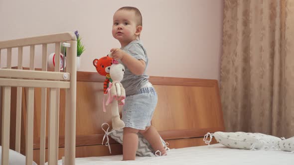 Newborn girl 12-17 months old plays with knitted toys tiger and hare standing on the parent's bed