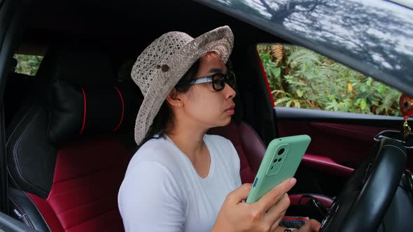 Asian female traveler uses a GPS navigation map on her smartphone while sitting in a car.