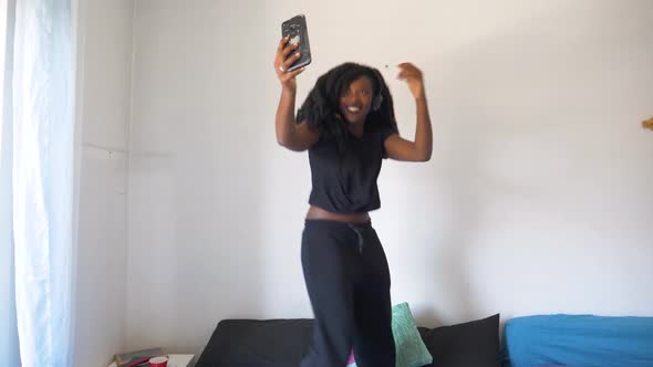 Slow motion shot of young woman dancing and using smartphone on bed