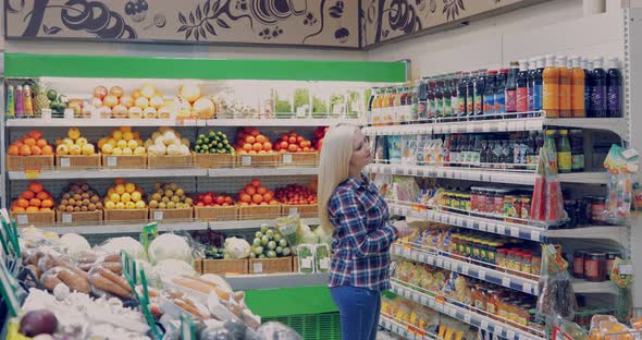 Attractive Woman is Walking Near the Supermarket Shelf and Selects the Products