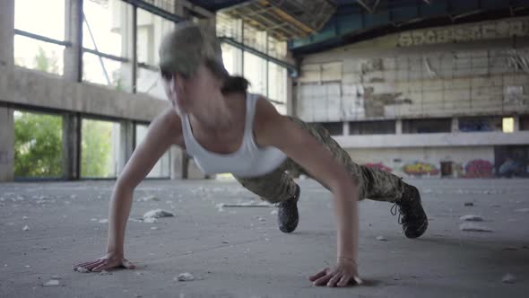 Confident Strong Young Woman in Military Uniform Push-ups in a Deserted Factory