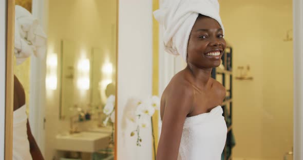 Portrait of smiling african american woman next to mirror with towel in bathroom