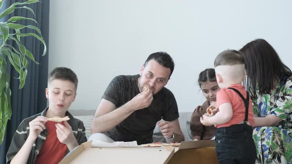 Happy Family Eating Pizza Sitting on Sofa at Home