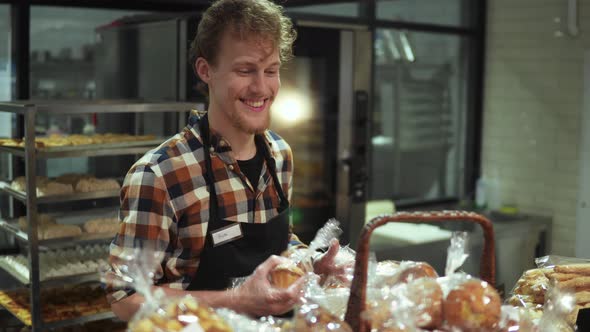 Positive Smiling Shop Clerk in Black Apron Putting Fresh Pastry Muffins on the Showcase Standing in