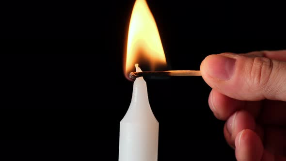 hand with a match lights a white wax candle, black background