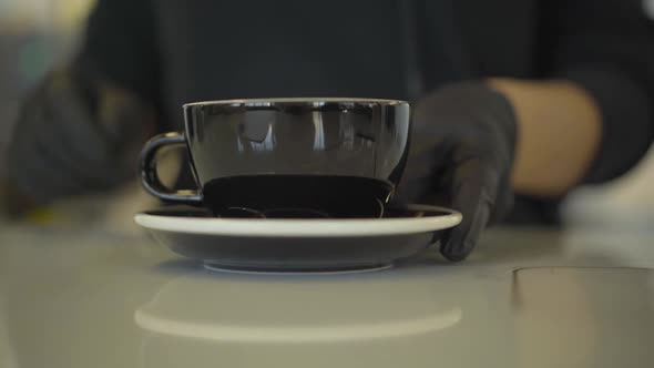 Unrecognizable Barista in Protective Gloves Approaching Coffee Cup To Camera. Close-up of Hot Drink