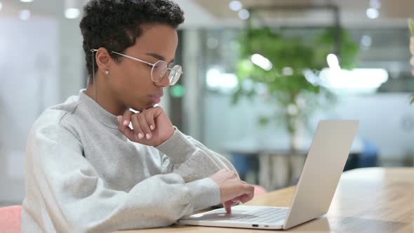 Casual African Woman Thinking and Working on Laptop 