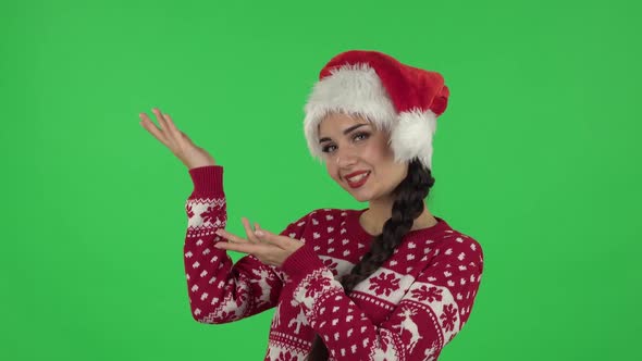 Portrait of Sweety Girl in Santa Claus Hat Is Talking and Pointing Side Hand for Something, Copy
