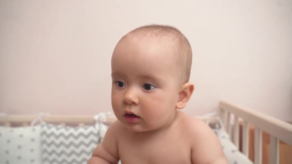 Portrait of a happy laughing newborn baby standing on his own feet in a crib.