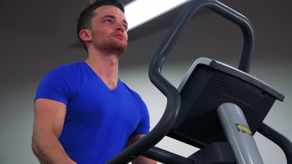 A Young Fit Man Trains on a Machine in a Gym - Closeup From Below