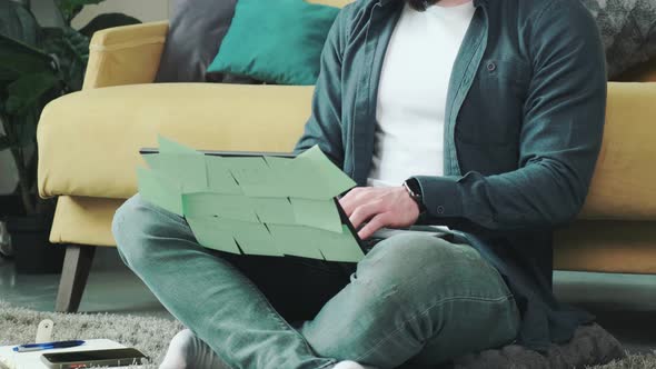 Man Working at the Computer with a Lot of Reminder Notes Sitting Near Sofa